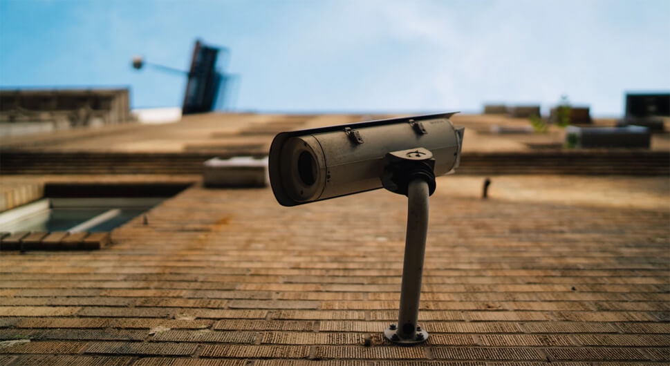 Security camera mounted on a brick wall, angled downwards under a clear blue sky.