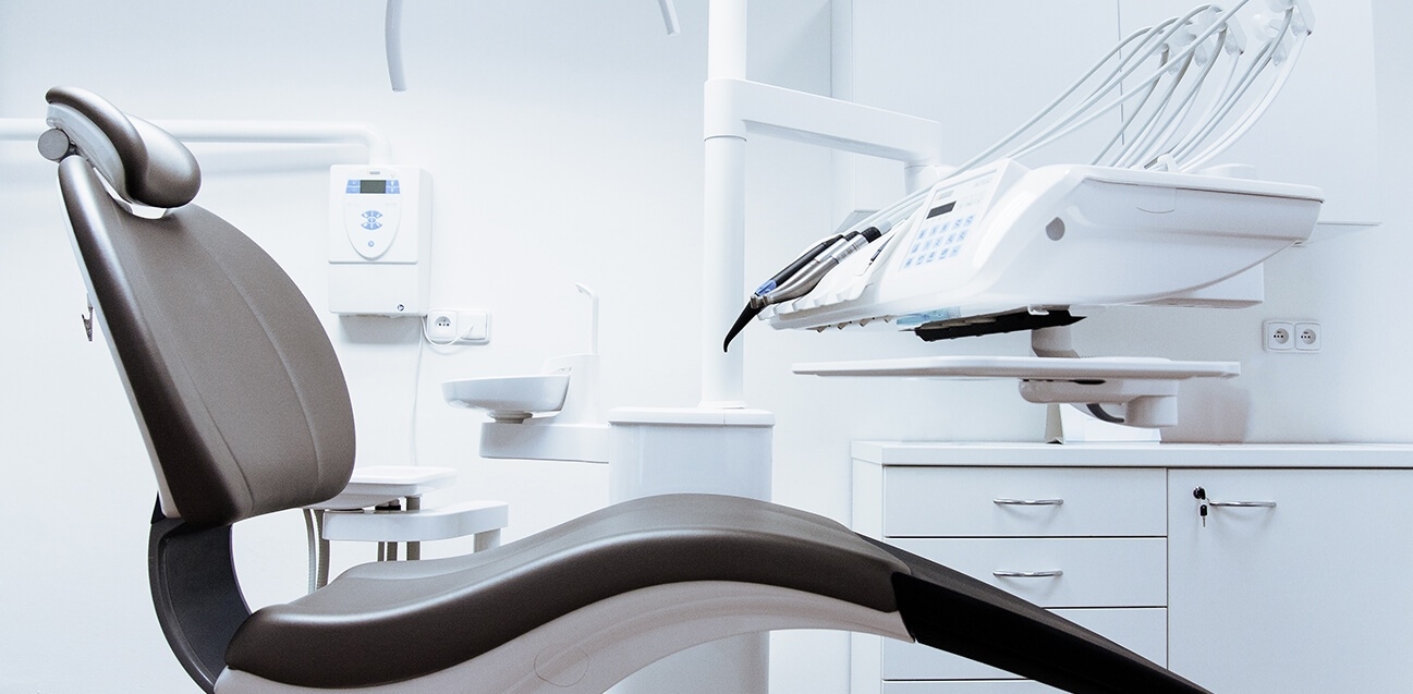 Dental clinic room with reclining patient chair and dental equipment on white walls.