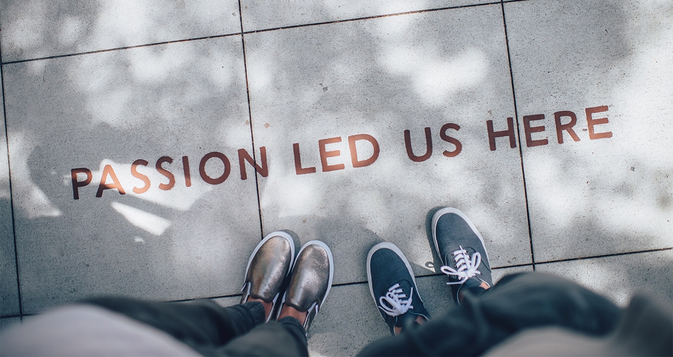 Two people standing on pavement with the text "PASSION LED US HERE" between them.