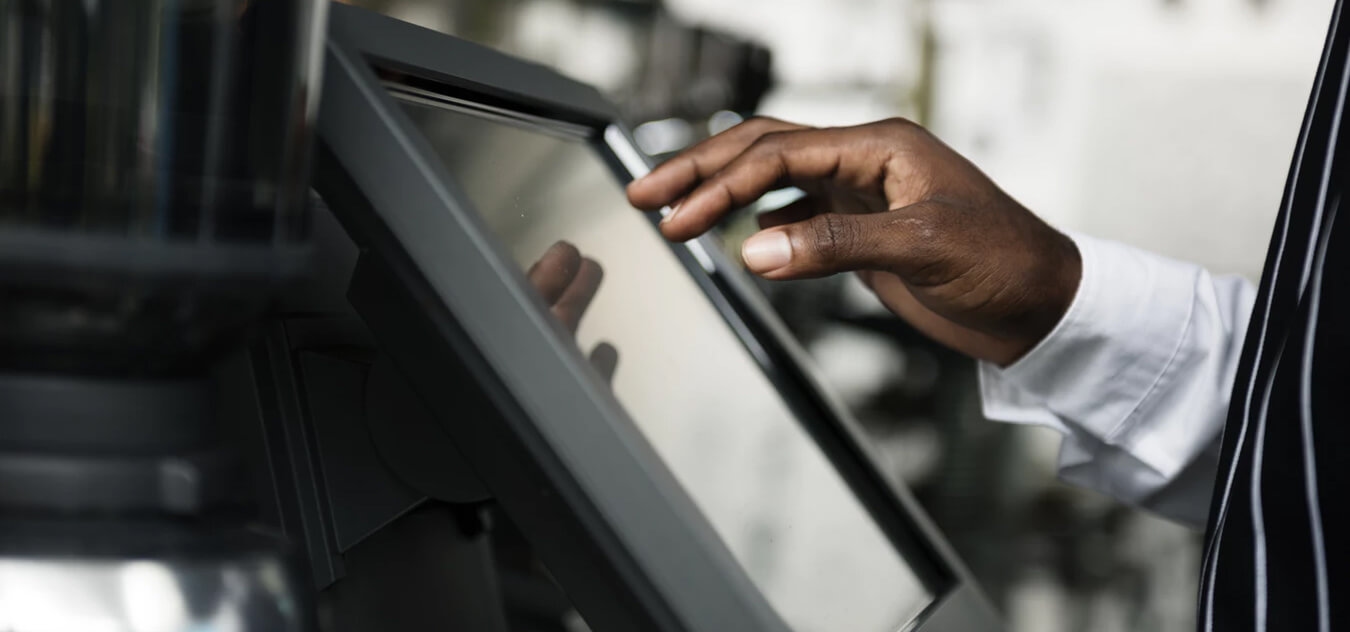 Hand of a person in a white shirt using a touchscreen device, possibly a POS system.