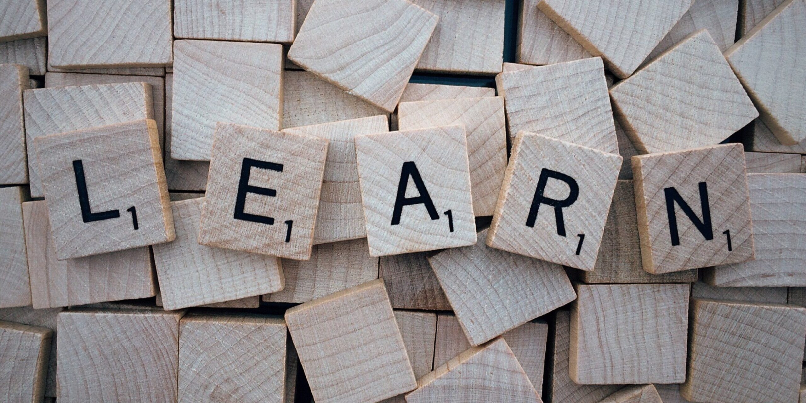 Wooden Scrabble tiles spelling the word "LEARN" on a pile of blank wooden tiles.