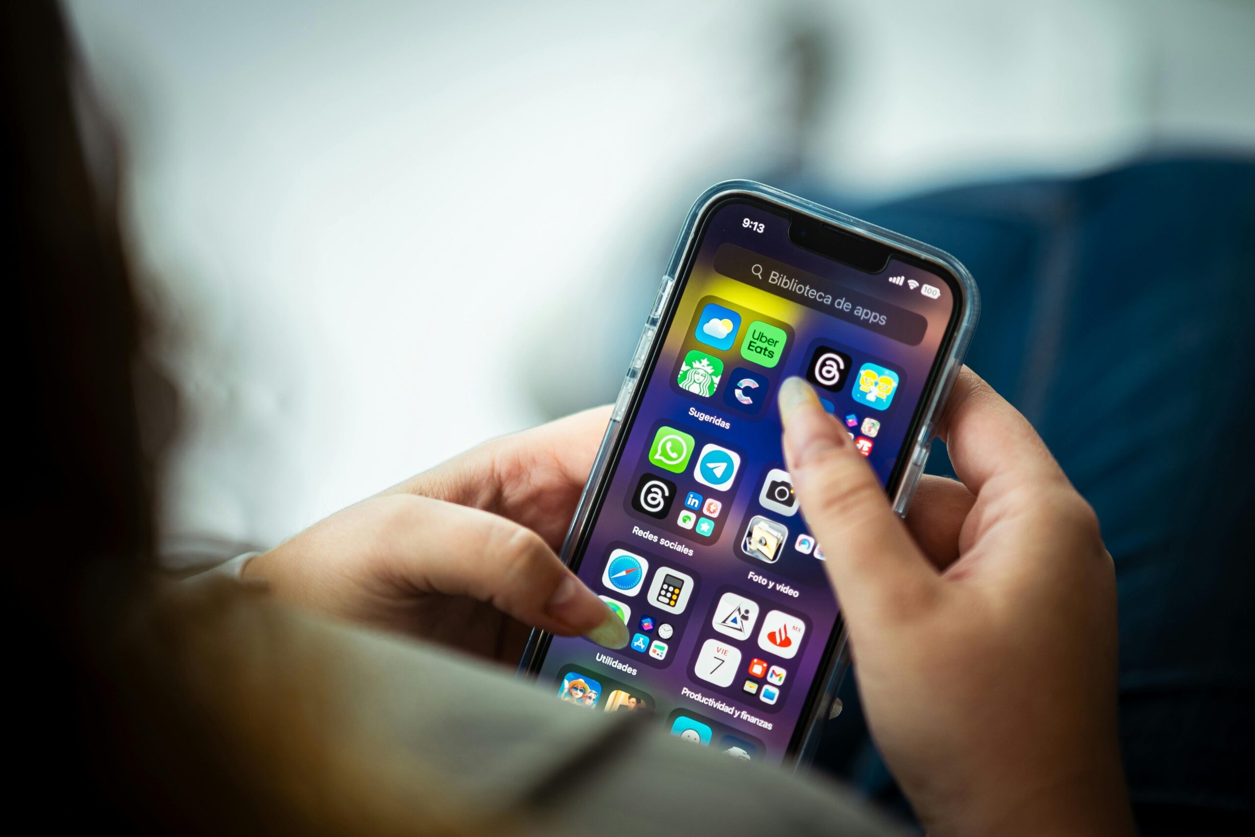 Person holding a smartphone displaying various app icons on the screen with a finger tapping.