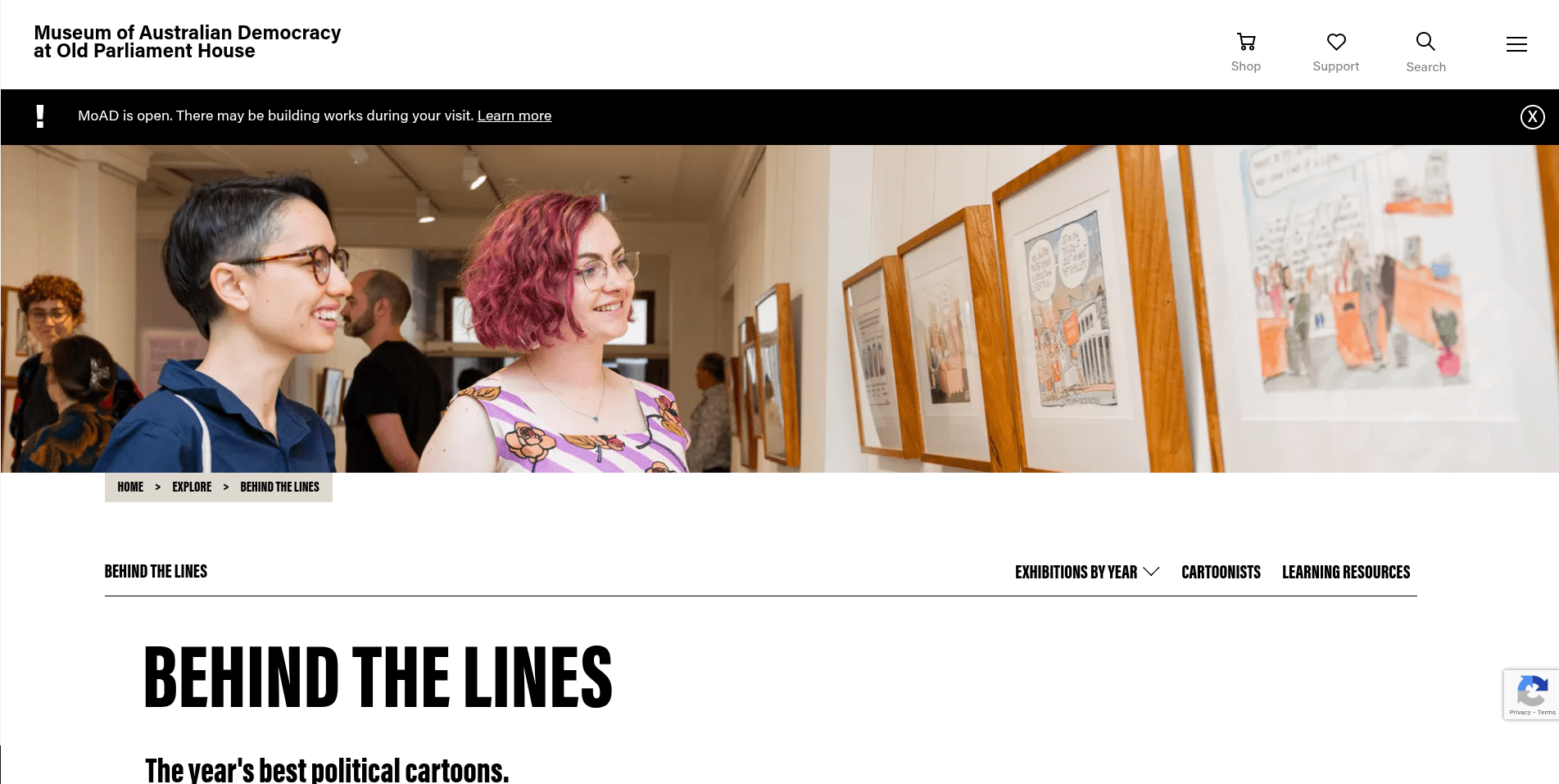 Two people smiling and viewing framed political cartoons in an art gallery.