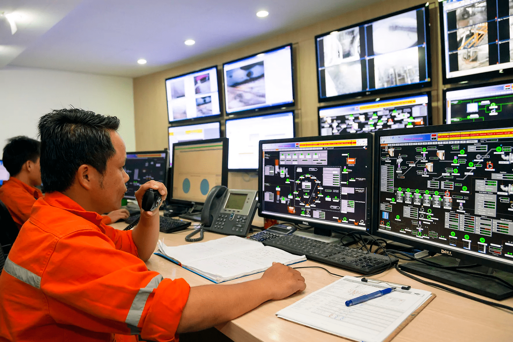 Operator monitoring industrial control systems on multiple computer screens in a control room.