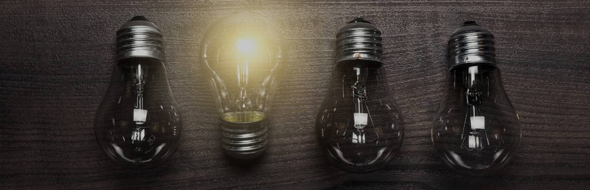 One glowing light bulb among four unlit bulbs, symbolizing a standout idea or innovation.